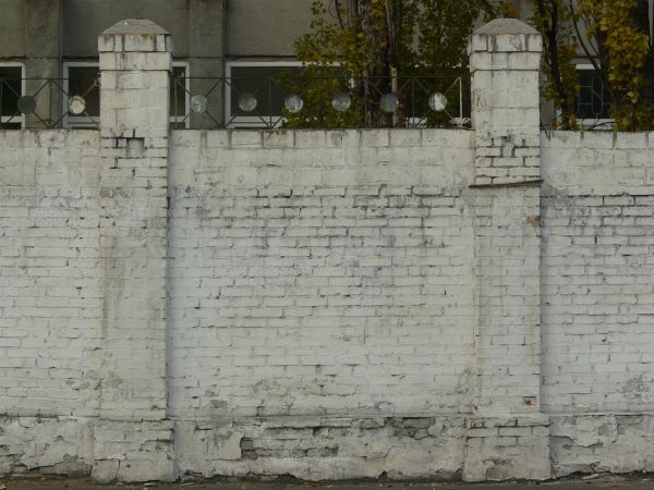 Brick fence texture made up of bricks painted white, with two tall columns made up of similar bricks. Bricks are in various degrees of relief and states of erosion.